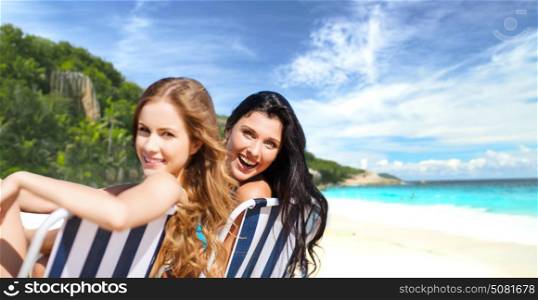 summer holidays, people, leisure, vacation and travel concept - happy women sunbathing on folding chairs over exotic tropical beach background. happy women sunbathing on chairs over summer beach