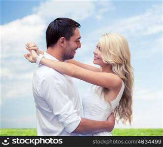 summer holidays, people, love and dating concept - happy couple hugging over blue sky and grass background