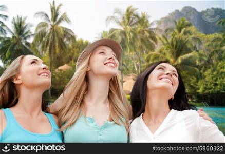 summer holidays, people, travel and vacation concept - happy young women looking up over resort beach with palm trees background
