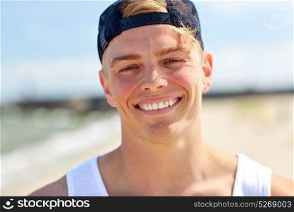 summer holidays, portrait and people concept - close up of happy smiling young man in cap on beach. close up of smiling young man on summer beach