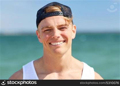 summer holidays, portrait and people concept - close up of happy smiling young manin cap on beach. close up of smiling young man on summer beach