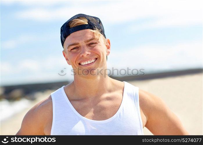 summer holidays, portrait and people concept - happy smiling young man in cap on beach. smiling young man on summer beach