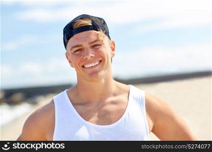 summer holidays, portrait and people concept - happy smiling young man in cap on beach. smiling young man on summer beach