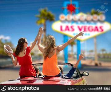 summer holidays, road trip and travel concept - happy friends driving in convertible car and waving hands over welcome to fabulous las vegas sign background. friends driving in convertible car at las vegas. friends driving in convertible car at las vegas
