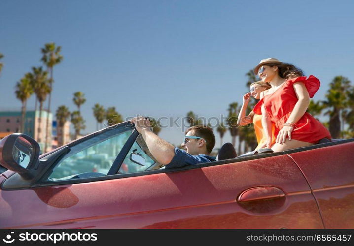 summer holidays, road trip and travel concept - happy friends driving in convertible car over venice beach background in california. friends driving in convertible car at venice beach