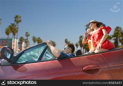 summer holidays, road trip and travel concept - happy friends driving in convertible car over venice beach background in california. friends driving in convertible car at venice beach