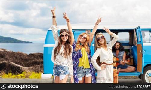 summer holidays, road trip, travel and people concept - happy young hippie friends showing peace hand sign and posing at minivan car over island background. happy hippie friends at minivan car on island