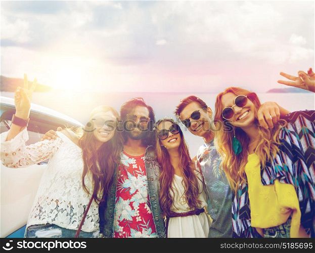 summer holidays, road trip, travel and people concept - smiling young hippie friends at minivan car showing peace hand sign over sea background. hippie friends at minivan car showing peace sign