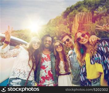 summer holidays, road trip, travel and people concept - smiling young hippie friends at minivan car showing peace hand sign over island background. hippie friends at minivan car showing peace sign