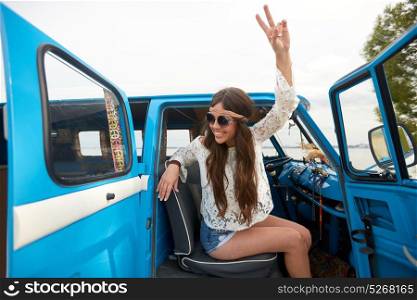 summer holidays, road trip, travel and people concept - smiling young hippie woman showing peace gesture in minivan car. happy hippie woman showing peace in minivan car