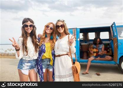 summer holidays, road trip, travel and people concept - smiling young hippie friends near minivan car showing peace hand sign at seaside. hippie friends near minivan car showing peace sign