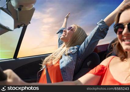 summer holidays, road trip, vacation, travel and people concept - happy young women driving in convertible car and laughing over sky background. happy young women driving in convertible car