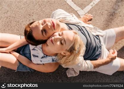 summer holidays, romantic and people concept - happy young couple sitting back to back on basketball playground. happy couple sitting on basketball playground