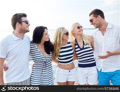summer, holidays, sea, tourism and people concept - group of smiling friends in sunglasses talking on beach