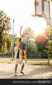 summer holidays, sport and people concept - happy young couple with ball playing on basketball playground. happy couple playing on basketball on playground