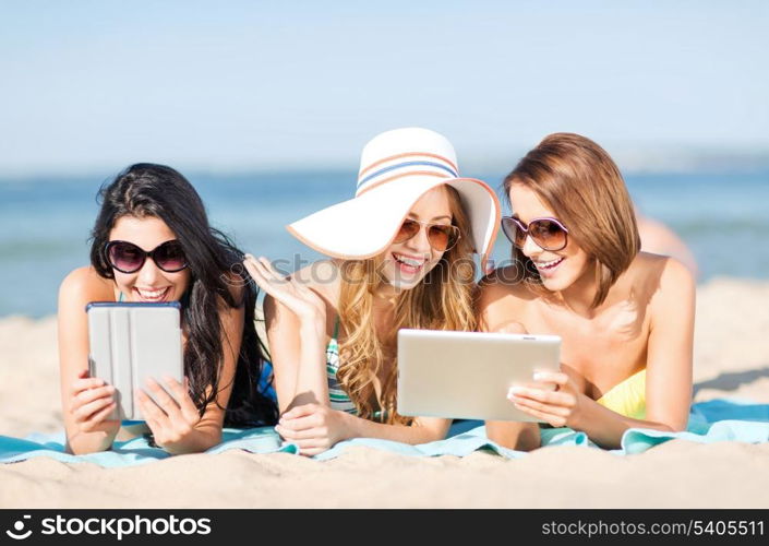 summer holidays, technology and internet concept - girls in bikinis with tablet pc sunbathing on the beach