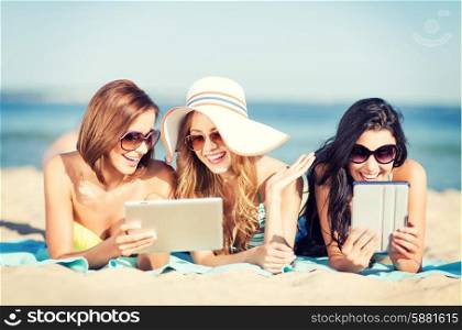 summer holidays, technology and internet concept - girls in bikinis with tablet pc sunbathing on the beach