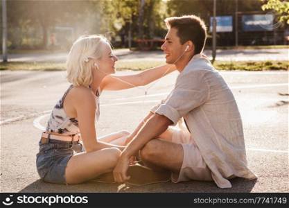 summer holidays, technology and people concept - happy couple with earphones listening to music on basketball playground. happy couple with earphones listening to music