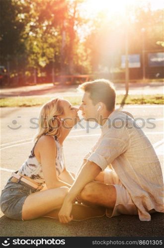 summer holidays, technology and people concept - happy couple with earphones listening to music and touching noses on basketball playground. happy couple with earphones listening to music