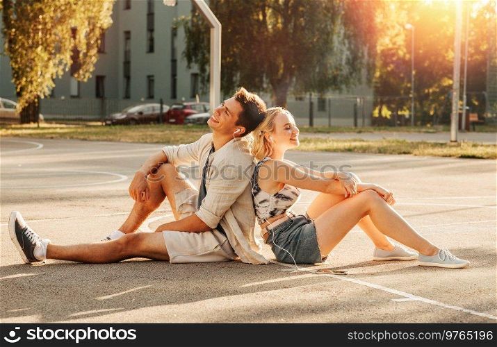summer holidays, technology and people concept - happy couple with smartphone and earphones listening to music on basketball playground. happy couple with smartphone and earphones in city