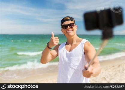 summer holidays, technology and people concept - happy smiling young man with smartphone taking selfie on beach. man with smartphone taking selfie on summer beach