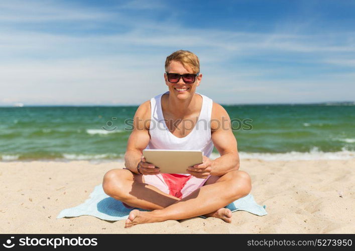 summer holidays, technology and people concept - happy smiling young man with tablet pc computer sunbathing on beach towel. happy smiling young man with tablet pc on beach