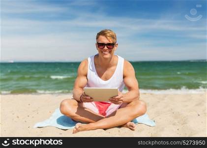 summer holidays, technology and people concept - happy smiling young man with tablet pc computer sunbathing on beach towel. happy smiling young man with tablet pc on beach
