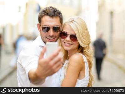 summer holidays, technology, love, relationship and dating concept - smiling couple taking picture with smartphone in the city