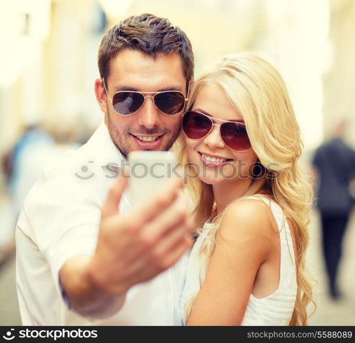 summer holidays, technology, love, relationship and dating concept - smiling couple taking picture with smartphone in the city