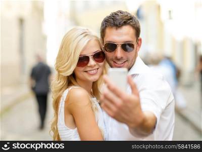 summer holidays, technology, love, relationship and dating concept - smiling couple taking picture with smartphone in the city