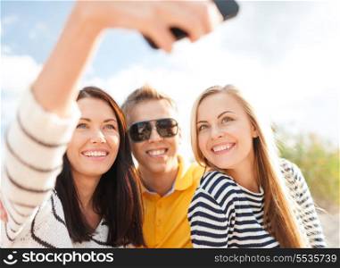 summer, holidays, technology, vacation and happiness concept - group of friends taking picture with smartphone camera
