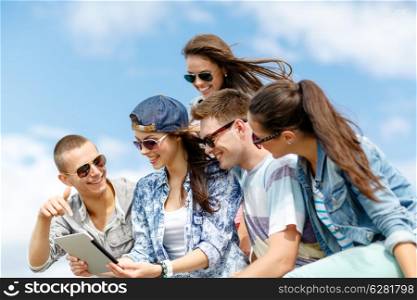 summer holidays, teenage and technology concept - group of teenagers looking at tablet pc computer outdoors