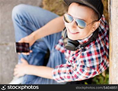 summer holidays, teenage and technology concept - teenager with headphones and smartphone outside