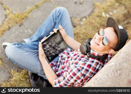 summer holidays, teenage and technology concept - teenager with headphones and tablet pc outside