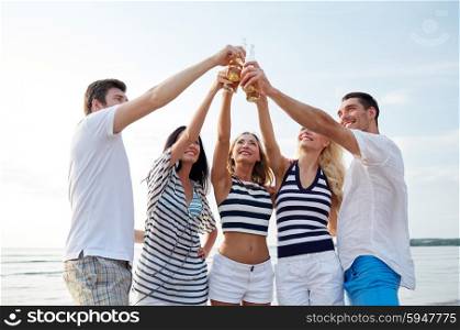 summer, holidays, tourism, drinks and people concept - group of smiling friends clinking bottles of beer or cider on beach