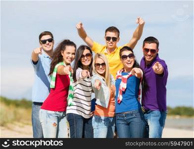 summer holidays, tourism, travel, gesture and people concept - group of happy friends in sunglasses pointing at you on beach