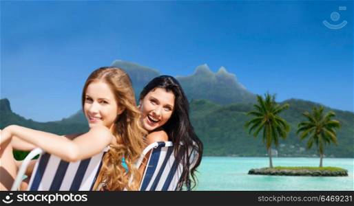 summer holidays, tourism, vacation and travel concept - happy women sunbathing in chairs at touristic resort over exotic bora bora island beach background. happy women sunbathing in chairs on exotic beach