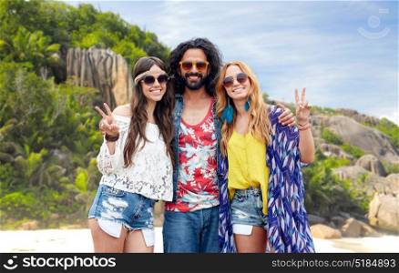 summer holidays, travel and people concept - smiling young hippie friends in sunglasses showing peace hand sign over tropical island beach background. happy hippie friends showing peace on island beach