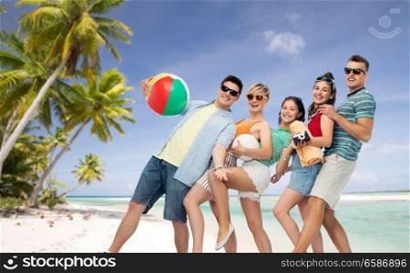 summer holidays, travel and vacation concept - group of happy smiling friends in sunglasses with ball, volleyball, towel and camera over tropical beach background in french polynesia. friends with beach supplies over exotic landscape