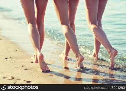 summer holidays, travel, body care and people concept - close up of happy young women walking and hugging on beach from back