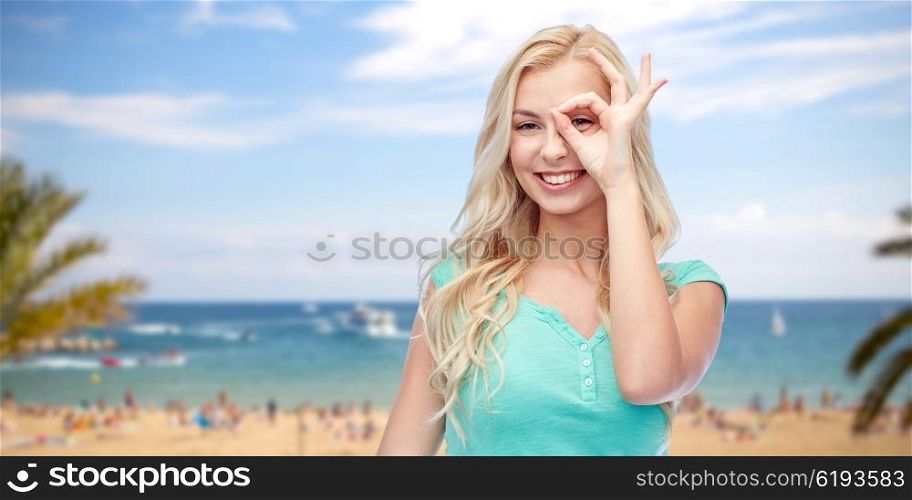 summer holidays, travel, emotions, expressions and people concept - smiling young woman or teenage girl making ok hand gesture over exotic tropical beach with palm trees and sea background