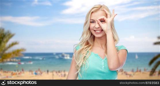 summer holidays, travel, emotions, expressions and people concept - smiling young woman or teenage girl making ok hand gesture over exotic tropical beach with palm trees and sea background