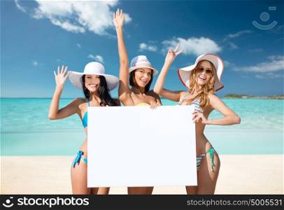 summer holidays, travel, people, advertisement and vacation concept - happy young women in bikinis holding white board over exotic tropical beach background. happy young women with white board on summer beach
