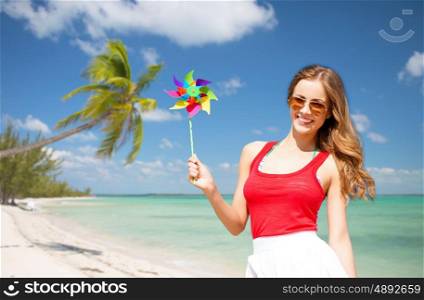summer holidays, travel, people and vacation concept - happy young woman in sunglasses with pinwheel over exotic tropical beach with palm trees and sea shore background