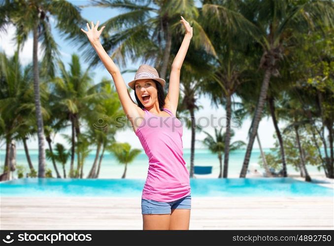 summer holidays, travel, people and vacation concept - happy young woman in hat over exotic tropical beach with palm trees and pool background