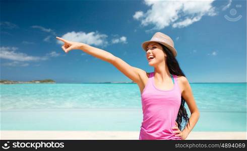 summer holidays, travel, people and vacation concept - happy young woman in hat pointing finger over exotic tropical beach background
