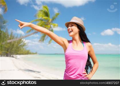 summer holidays, travel, people and vacation concept - happy young woman in hat pointing finger over exotic tropical beach with palm trees and sea shore background. happy young woman in hat on summer beach