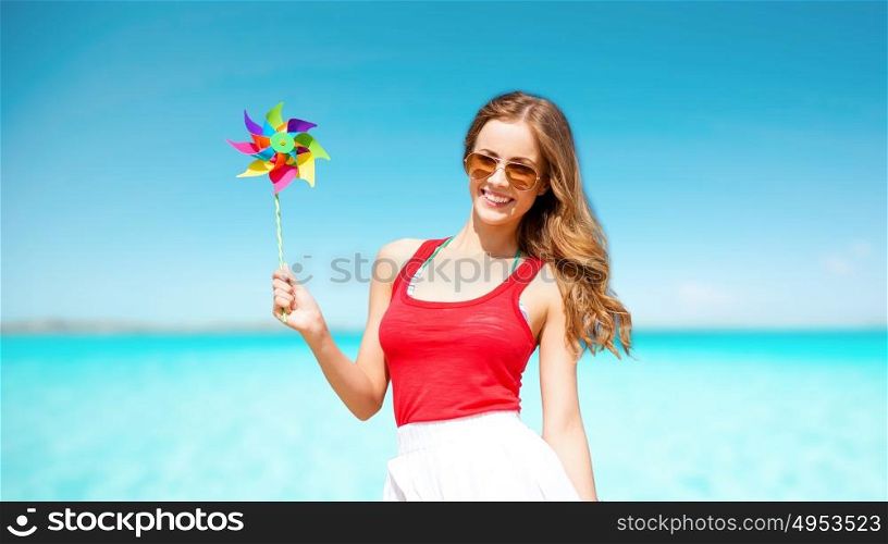 summer holidays, travel, people and vacation concept - happy young woman in sunglasses with pinwheel over blue sky and sea background. happy woman with pinwheel over blue sky and sea