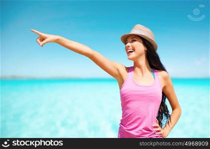 summer holidays, travel, people and vacation concept - happy young woman in hat pointing finger over sea and blue sky background. happy young woman in hat on summer beach
