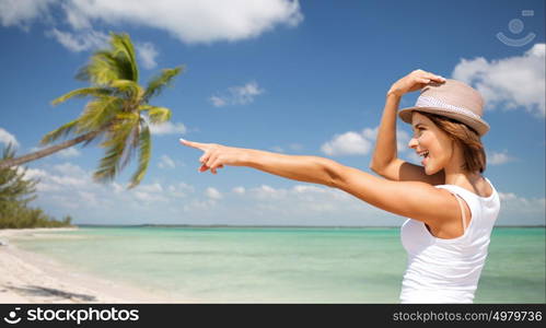 summer holidays, travel, people and vacation concept - happy young woman in hat pointing finger over exotic tropical beach with palm trees and sea shore background. happy young woman in hat on summer beach